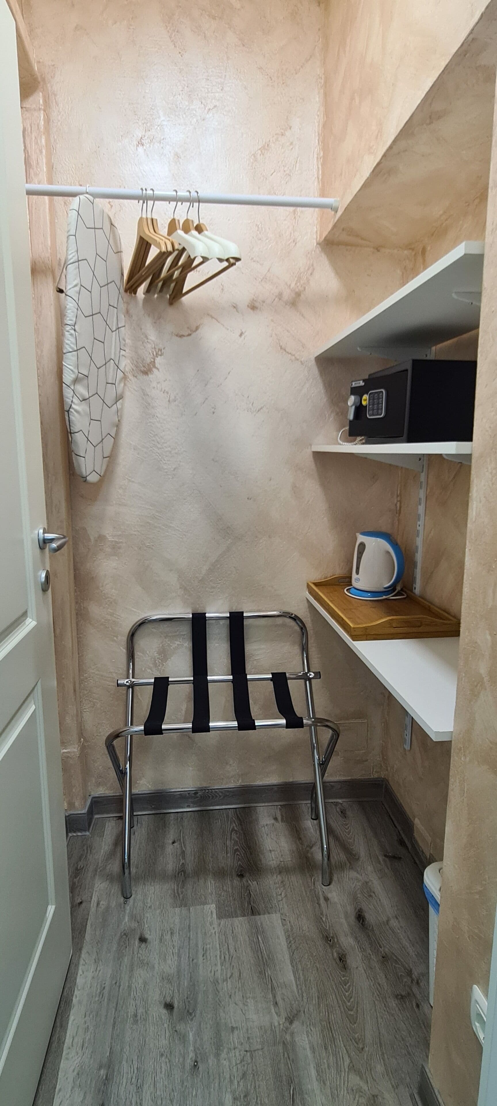 A small, compact room with a metal drying rack, a kettle on a shelf, and a door with a handle.
