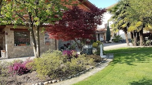 Ein Haus mit einer Steinauffahrt, ein gepflegter Garten mit verschiedenen Pflanzen und Blumen, und ein klarer Himmel.