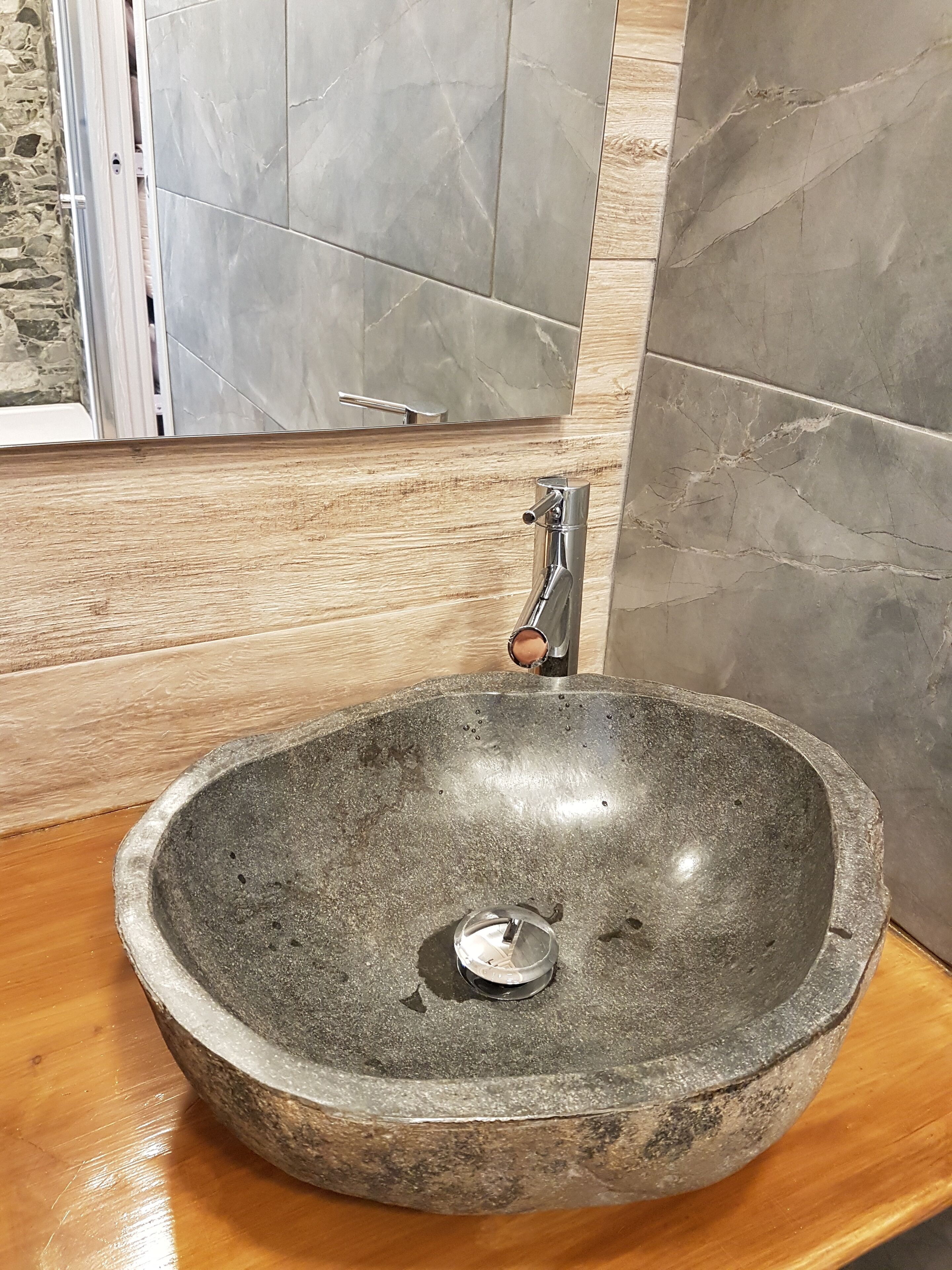 Un évier en pierre avec un robinet moderne, dans une salle de bain dotée d’un plancher en bois et de carreaux de marbre gris.