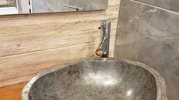 Un évier en pierre avec un robinet moderne, dans une salle de bain dotée d’un plancher en bois et de carreaux de marbre gris.