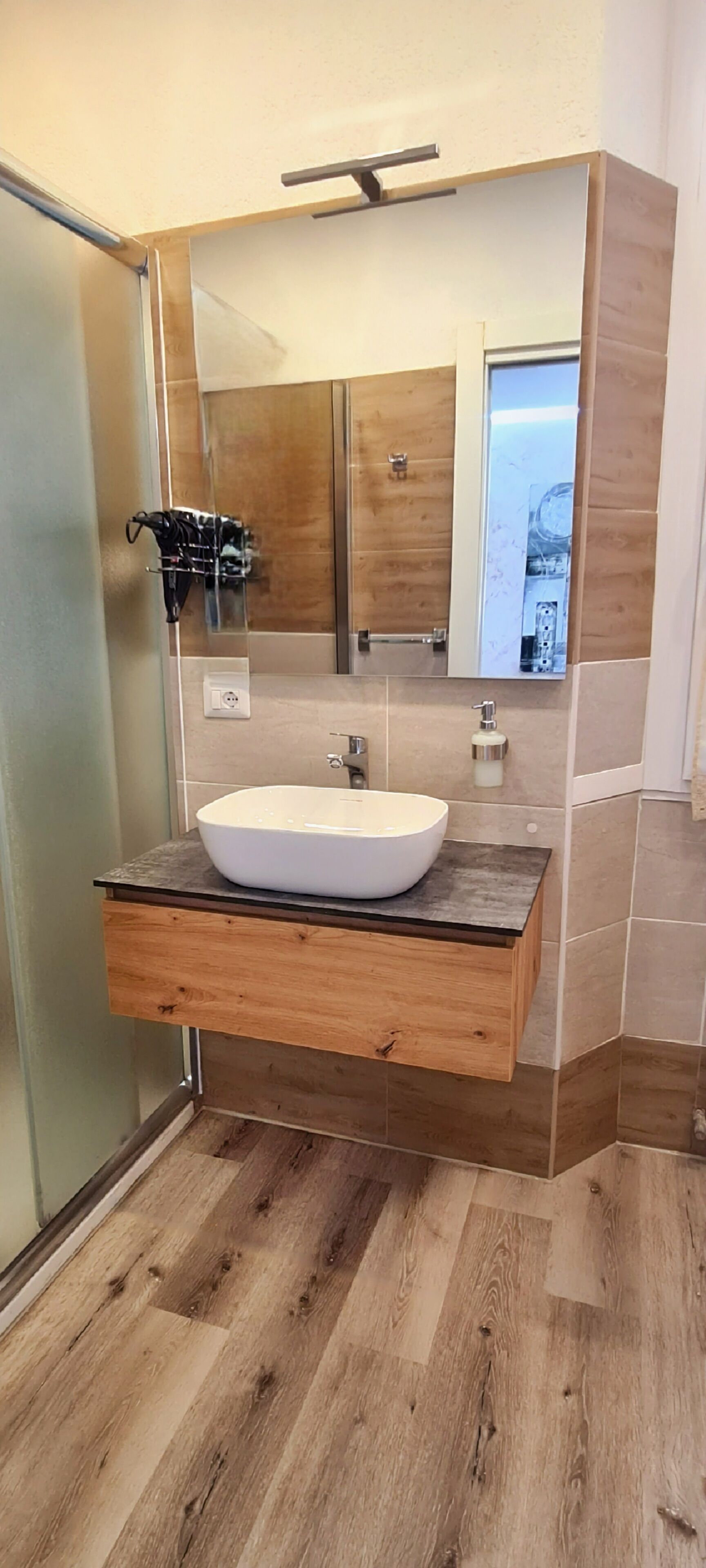 A bathroom with a wooden vanity, a white vessel sink, and a large mirror.