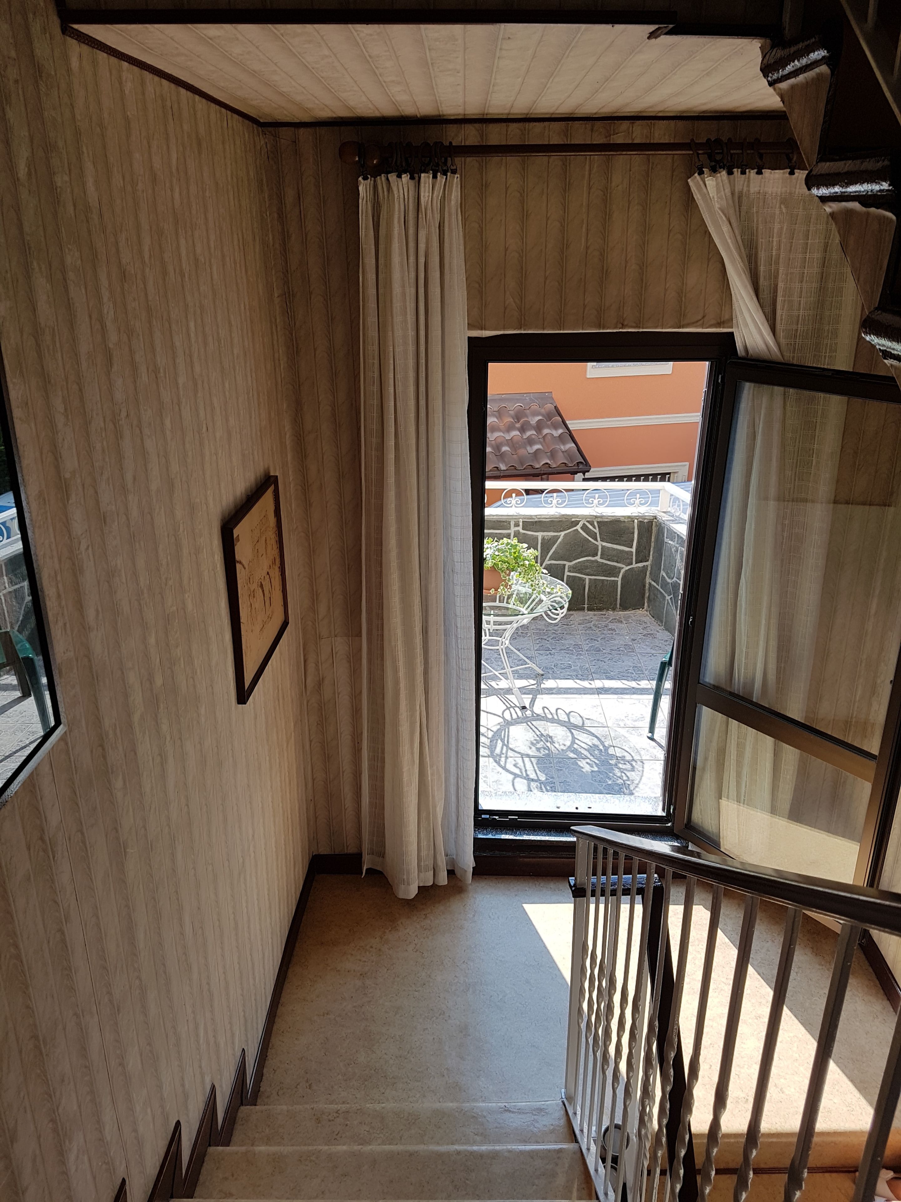 A staircase with a view of an outdoor patio area, a framed picture on the wall, and a window with curtains.