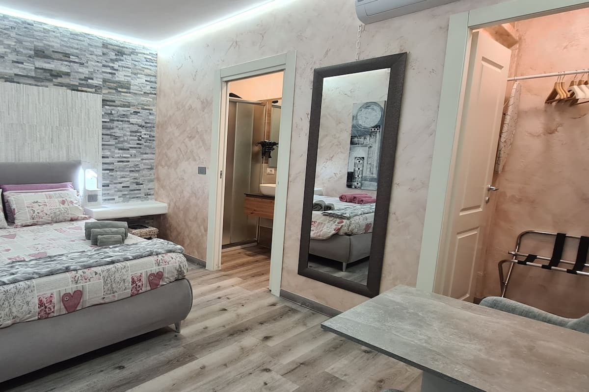 A modern bedroom with a large bed, bedside tables, a mirror, and a wooden floor.