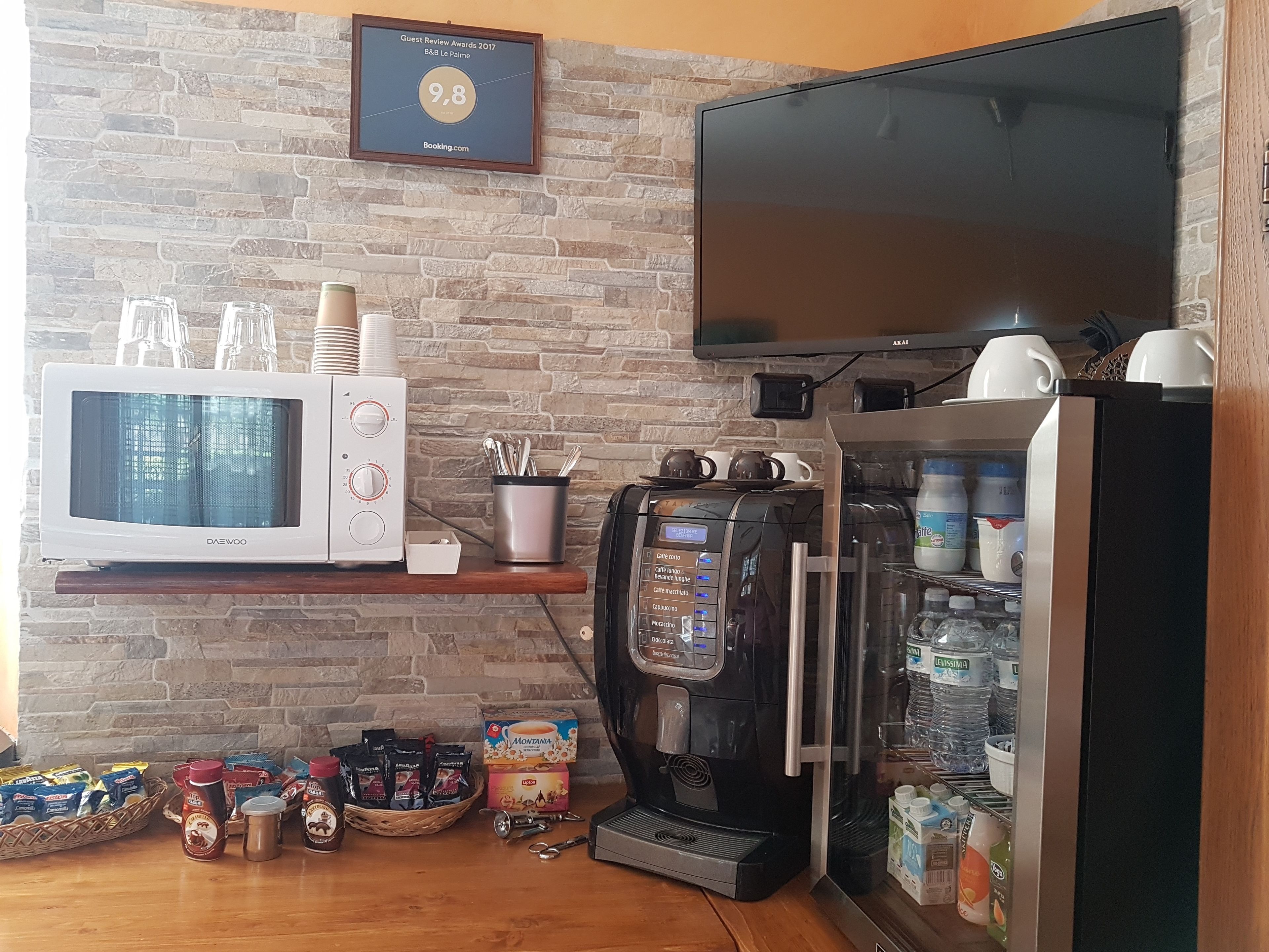 A kitchenette with a microwave, coffee machine, and a TV mounted on a brick wall.