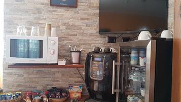 A kitchenette with a microwave, coffee machine, and a TV mounted on a brick wall.