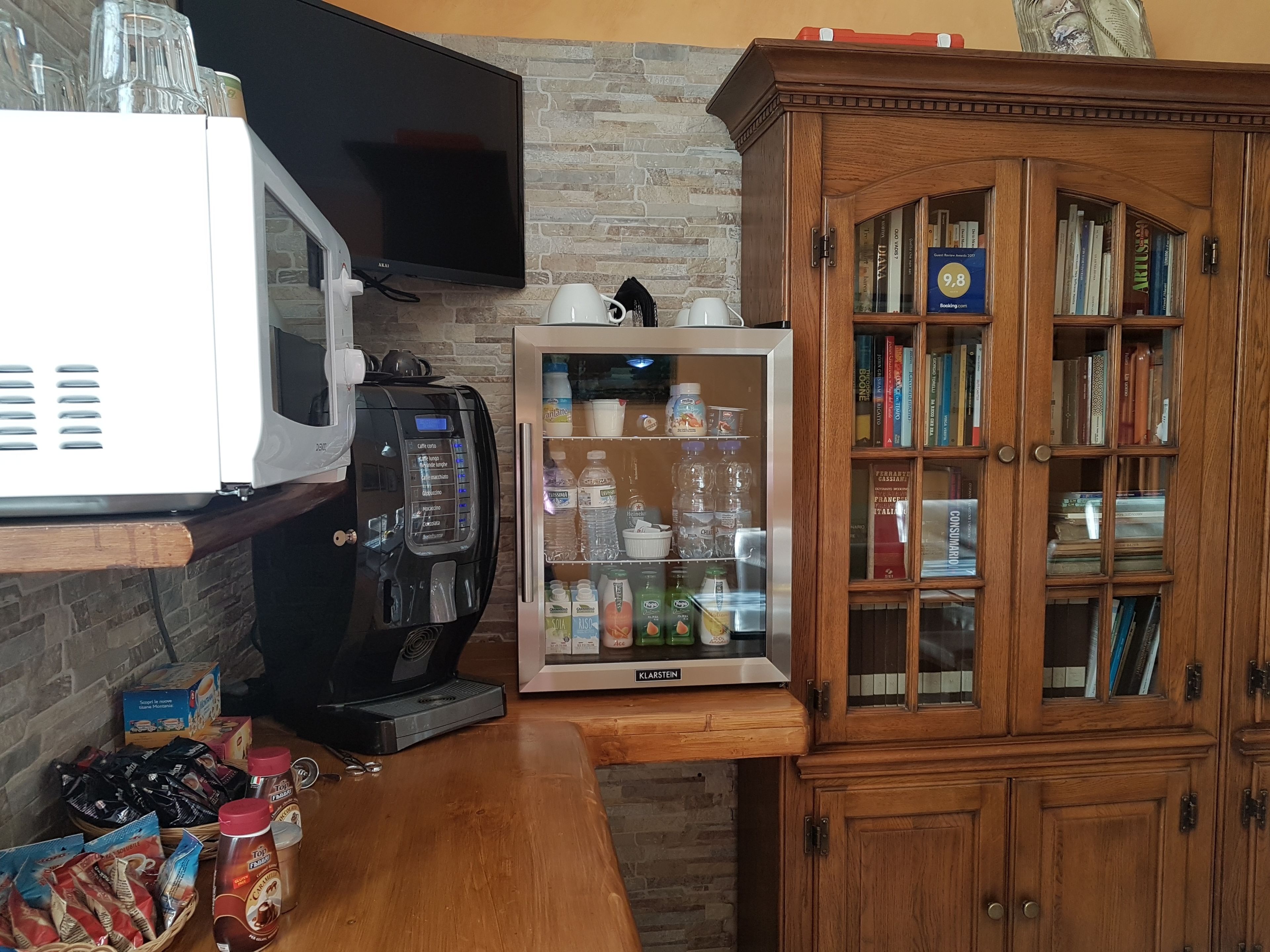 A kitchen with a microwave, coffee machine, refrigerator, and wooden cabinet with books.