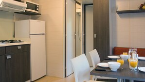 A modern kitchen with a refrigerator, stove, and microwave. There is a dining table with chairs and breakfast items like orange juice and a pitcher. - Camping Le Sous Bois (Saint-Maurice-d'Ibie)