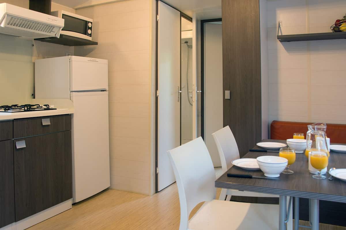 Una cocina moderna con refrigerador, estufa y microondas. Hay una mesa de comedor con sillas y artículos para el desayuno, como jugo de naranja y una jarrón.
