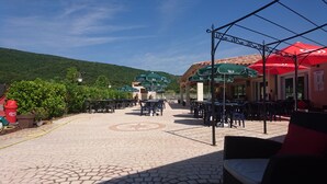 An outdoor patio area with tables and chairs, green umbrellas, and a tiled floor. - Camping Le Sous Bois (Saint-Maurice-d'Ibie)