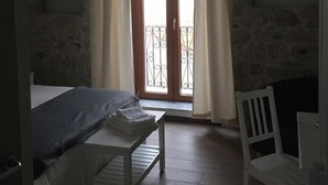 Ein Zimmer mit Bett, kleinem Tisch, Stuhl und einem Balkon mit Vorhängen.
