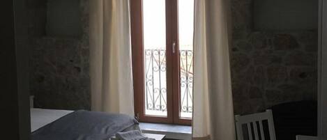 Una habitación con cama, una mesita, una silla y un balcón con cortinas.