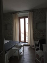 Una habitación con cama, una mesita, una silla y un balcón con cortinas.