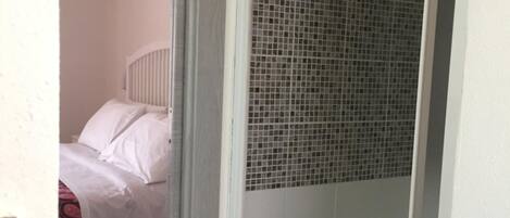 A room with a bed, a shower area with a tiled wall, and a white curtain.