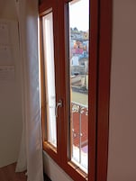 Una habitación con ventana de madera, cortina blanca y vistas a edificios coloridos.