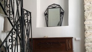 Eine Treppe mit aufwendigen schwarzen Metallgeländern, ein hölzerner Konsolentisch mit einem Spiegel darüber und eine Steinwand zur Rechten.