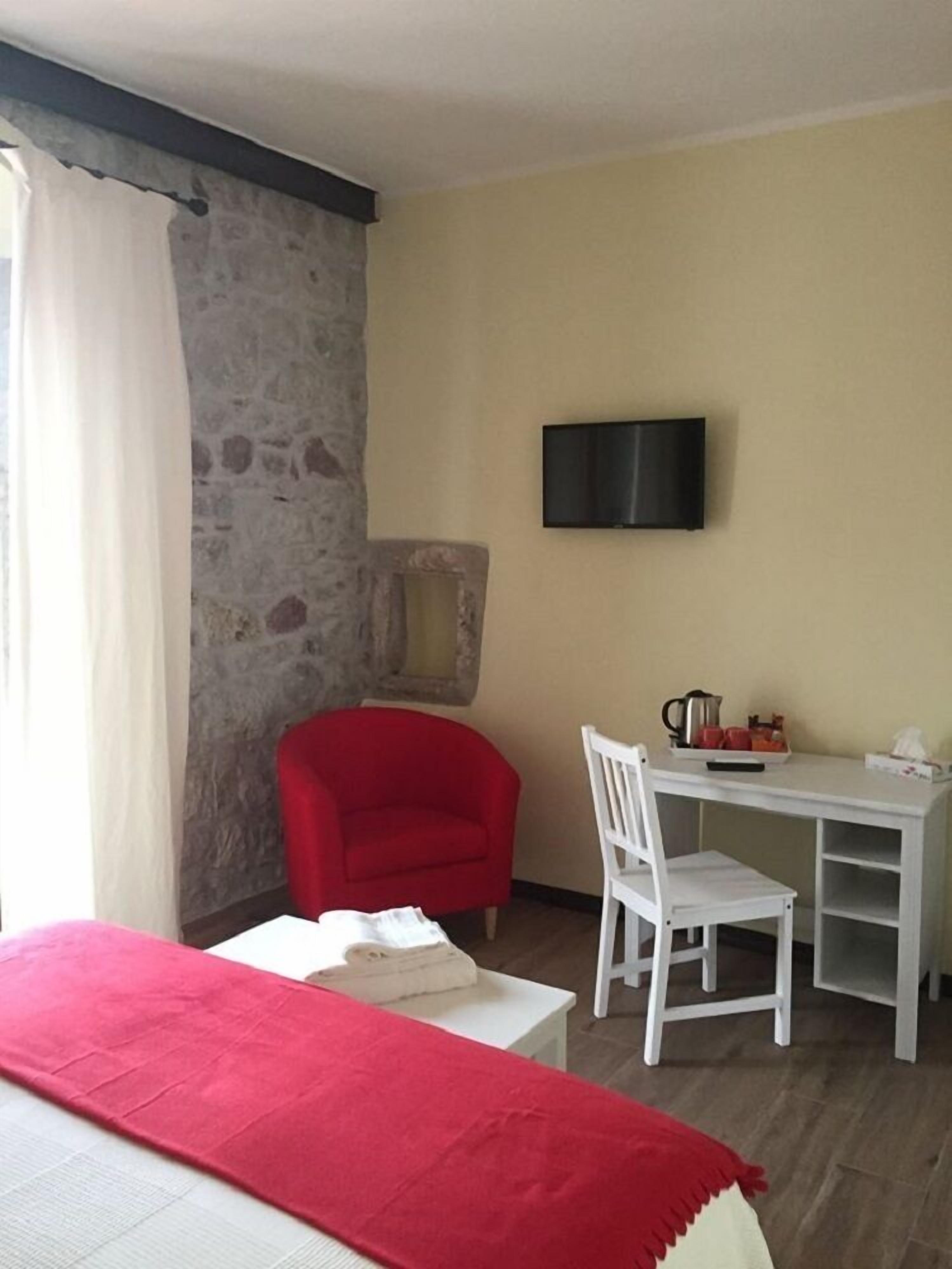 A room with a bed, a red chair, a white desk, and a television mounted on the wall.