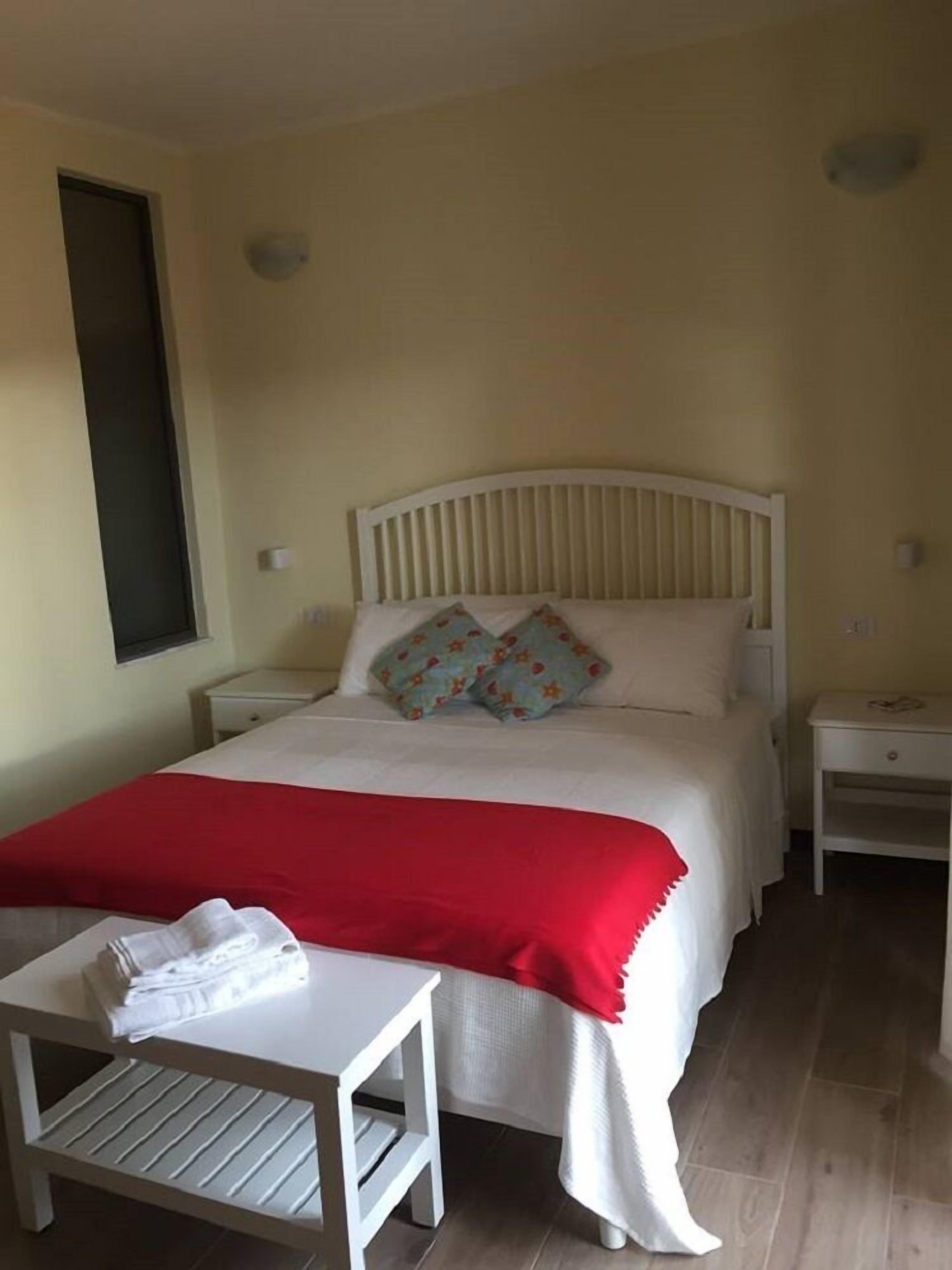 Quarto bem arrumado com cama, duas mesas de cabeceira, uma mesinha com toalhas e uma janela.