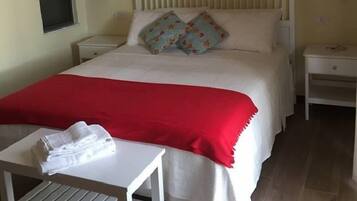 Quarto bem arrumado com cama, duas mesas de cabeceira, uma mesinha com toalhas e uma janela.