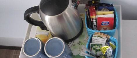 A tray with a silver mug, two blue cups, and a blue container holding food items and condiments.