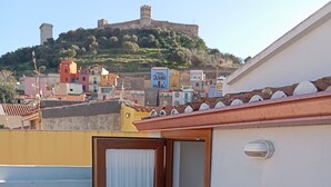 Ein Balkon mit einer Tür zu einem Zimmer, einem Fliesenboden und Blick auf einen Hügel mit Gebäuden.