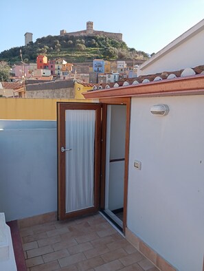 A balcony with a door leading to a room, a tiled floor, and a view of a hill with buildings. - Bomarosa Rooms (Bosa)