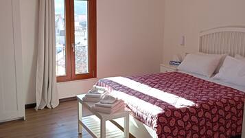 A bedroom with a bed, a bedside table with towels, a window with curtains, and a ceiling fan.