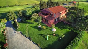 A two-story house with a red roof, surrounded by lush green fields and trees. - Agriturismo Fossederi (Santa Luce)