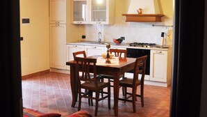 A kitchen with wooden beams, a dining table with chairs, and a red sofa. - Agriturismo Fossederi (Santa Luce)
