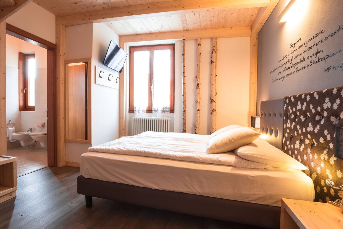 A bedroom with a bed, wooden headboard, a wall-mounted TV, and a window with curtains.