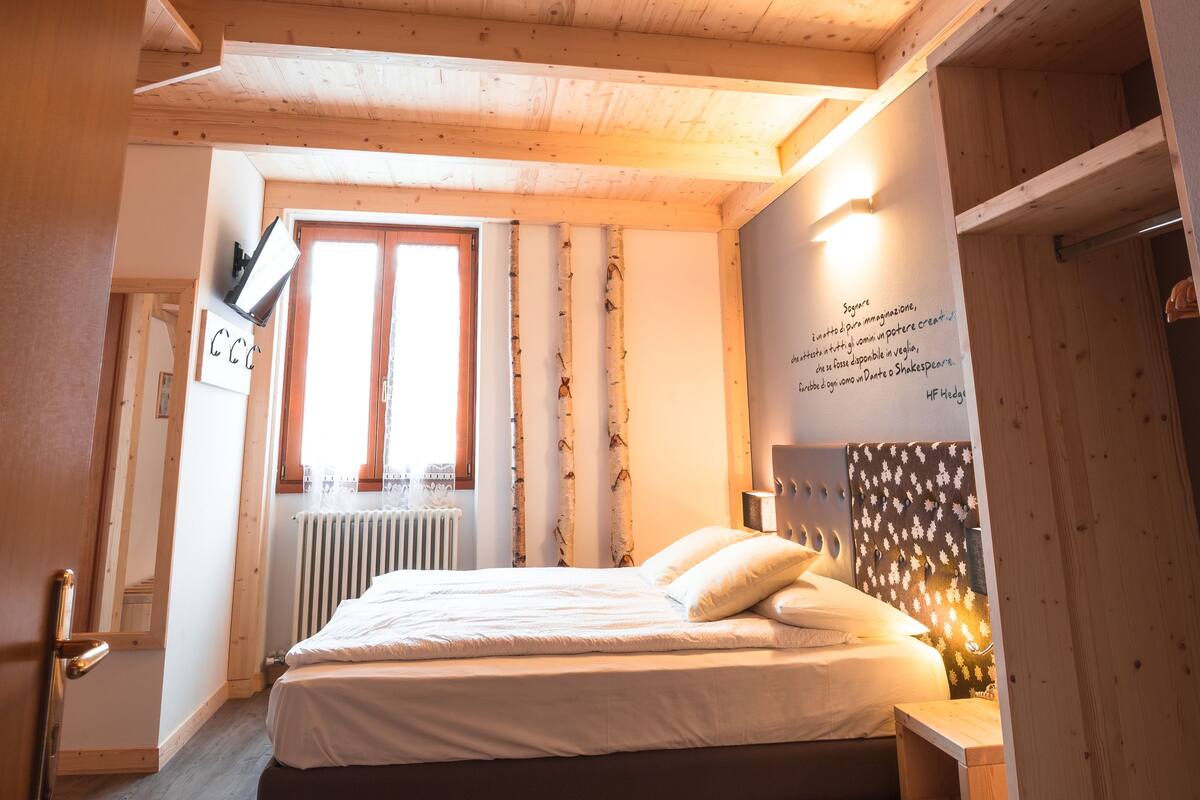A bedroom with a wooden ceiling, a bed, a nightstand, a window, and a wall with text.