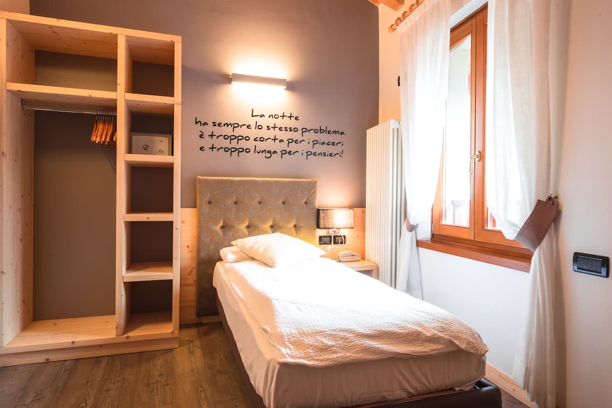 A bedroom with a bed, a wardrobe, a nightstand, and a wall-mounted light.