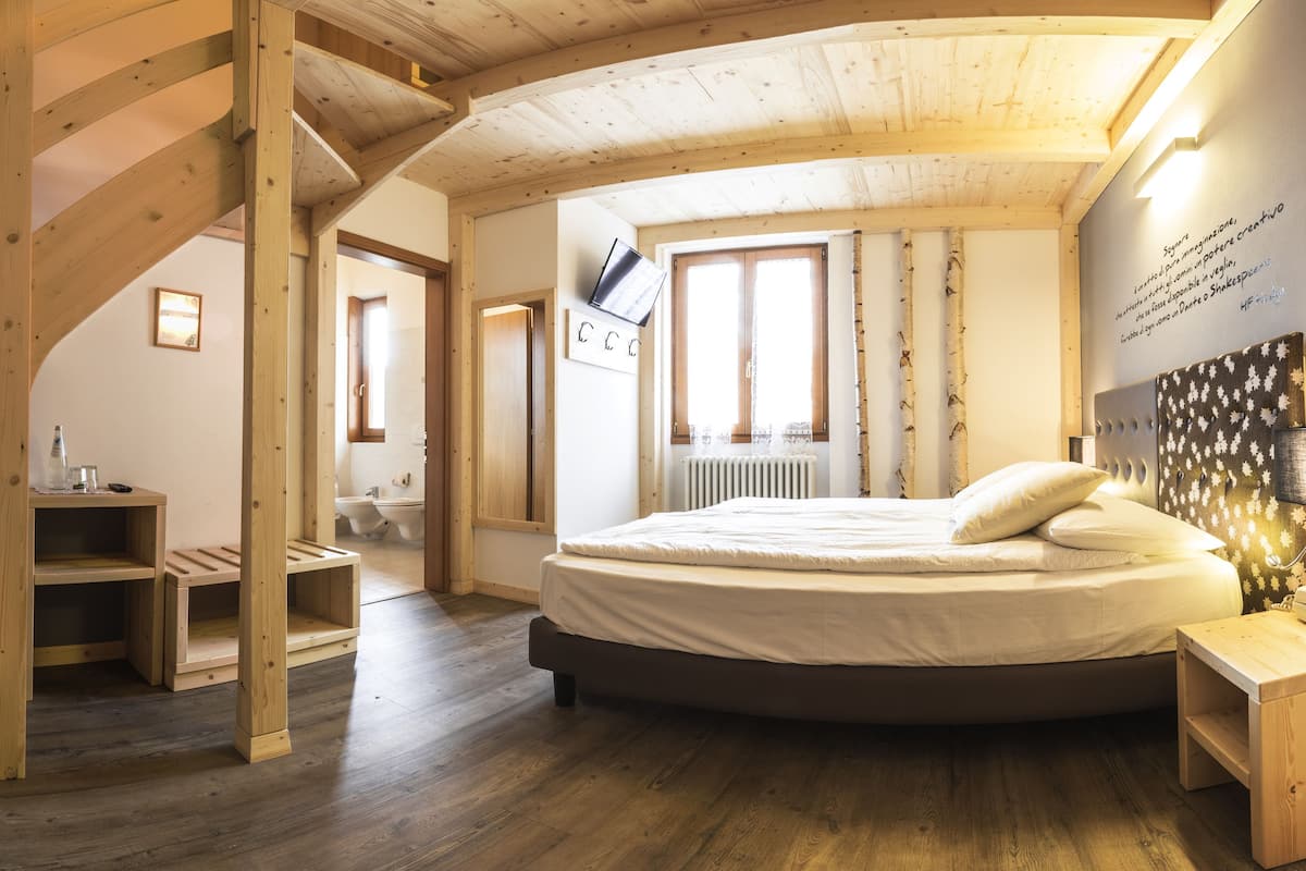 A bedroom with a wooden staircase, a round bed, and a view of a bathroom.