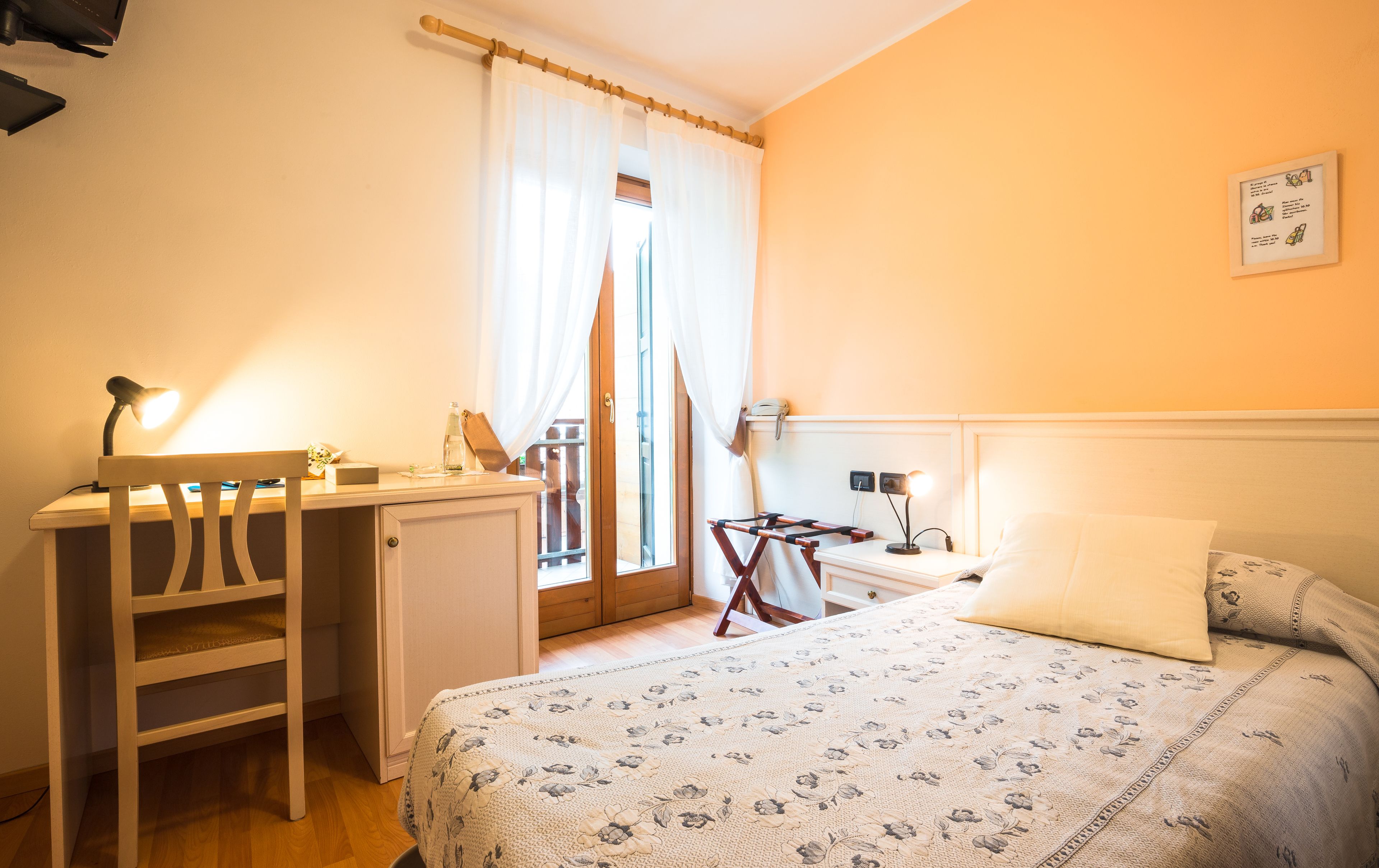 A bedroom with a bed, a desk, a chair, a small table, and a window with curtains.