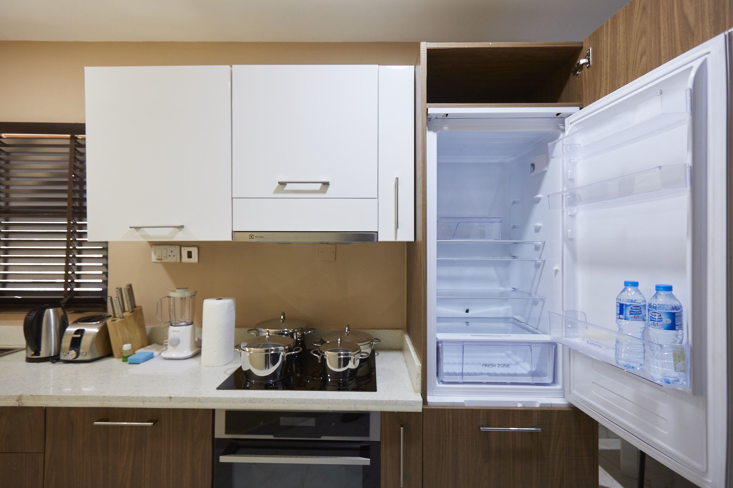 A kitchen with white cabinets, a countertop with a kettle, toaster, blender, and pots. The refrigerator is open, showing a water dispenser and a freezer.