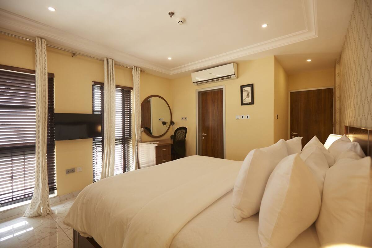 Une chambre à coucher avec un grand lit, une table de chevet, un miroir, un appareil de climatisation et une armoire.