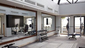 A gym with exercise equipment, a TV, and large windows. - Belanova Apartments & Suites (Abuja)