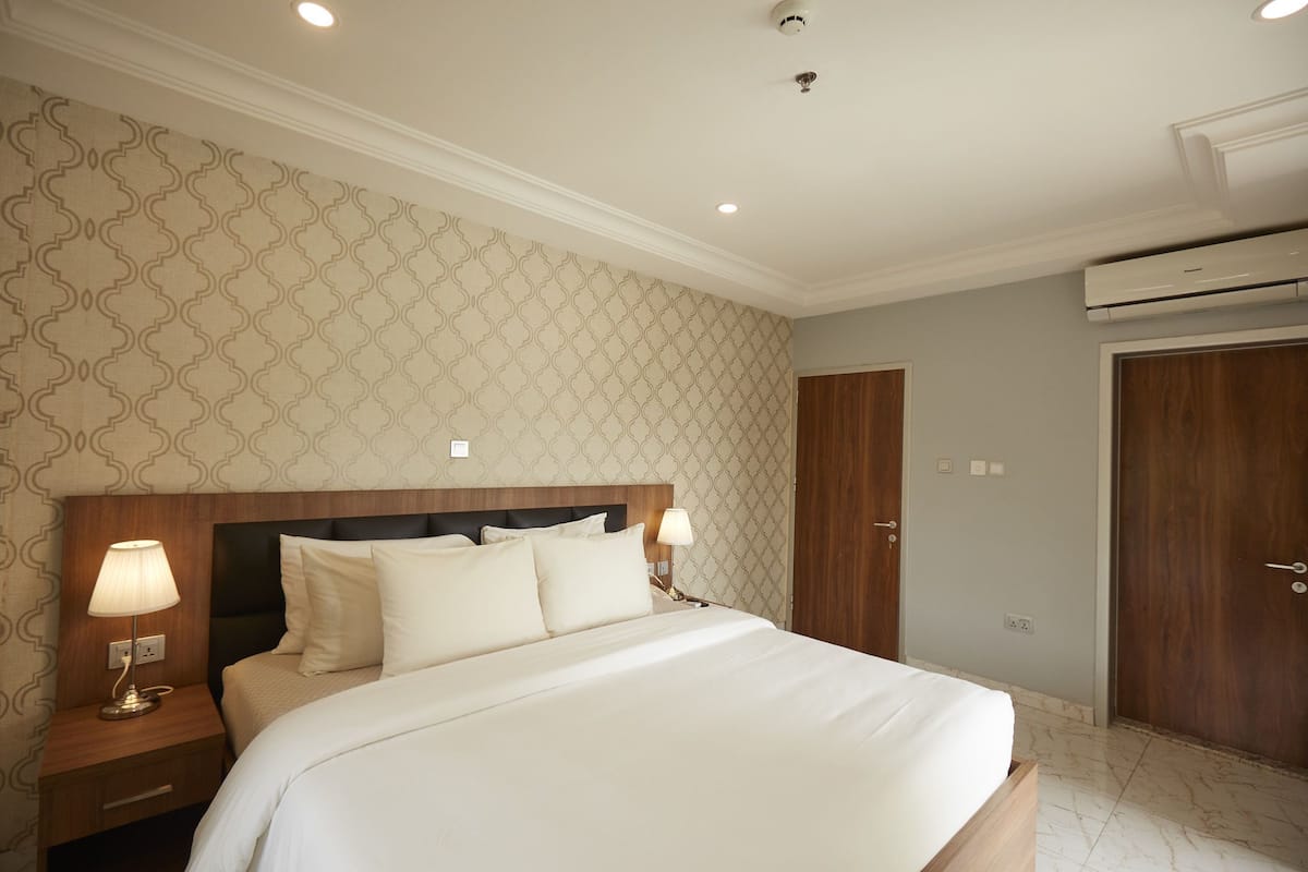 Une chambre d’hôtel comprenant un lit, des tables de chevet, une lampe, une tête de lit, un mur orné d’un motif géométrique, un appareil de climatisation et une porte.