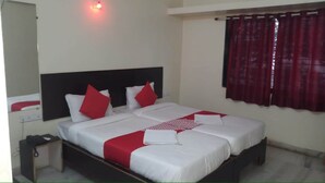 A double bed with white and red bedding, a black headboard, and a red curtain on the window. - Arjun Pride Hotel (Baramati)
