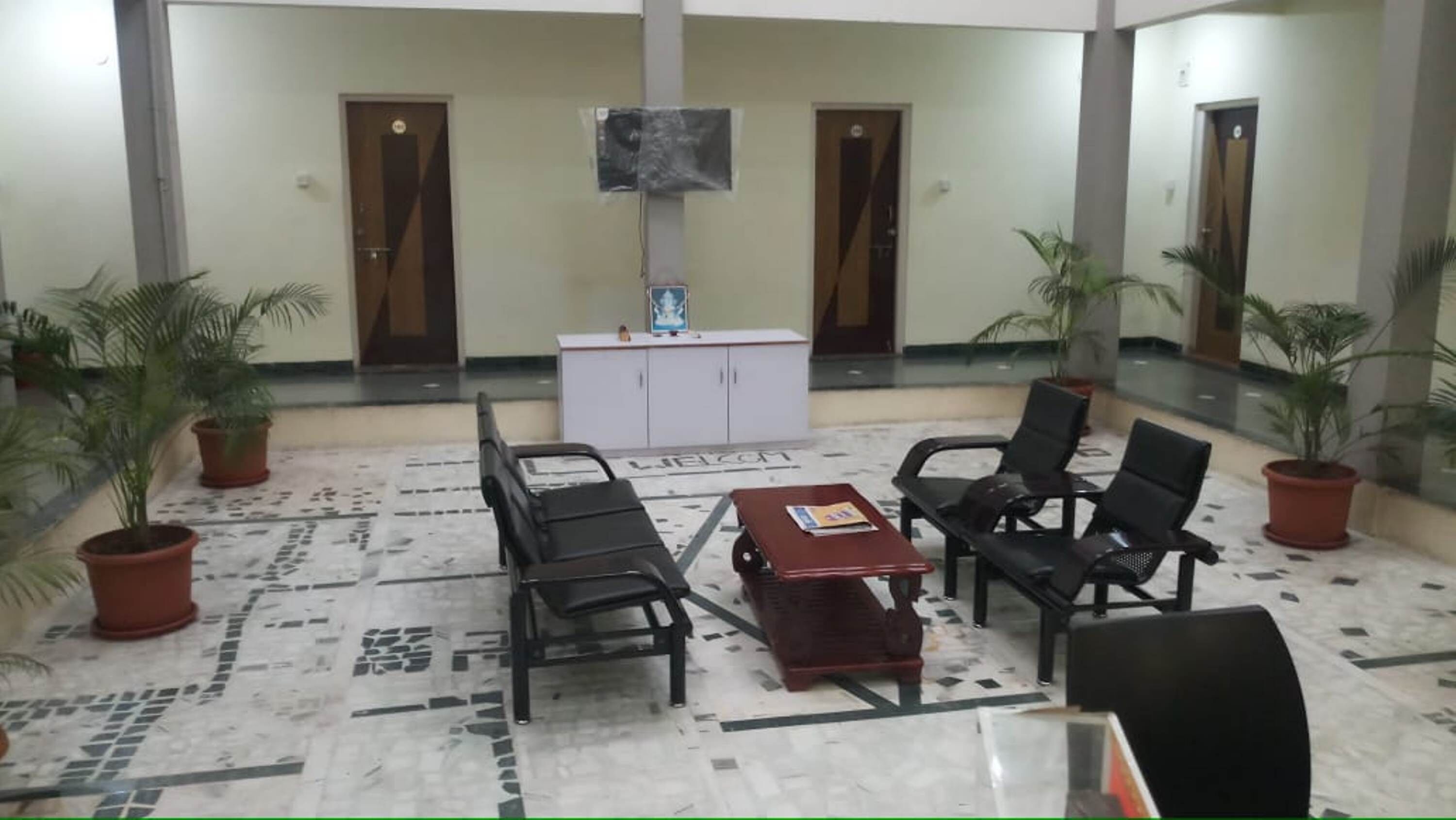 A lobby with a reception desk, two black chairs, a red table, and potted plants.