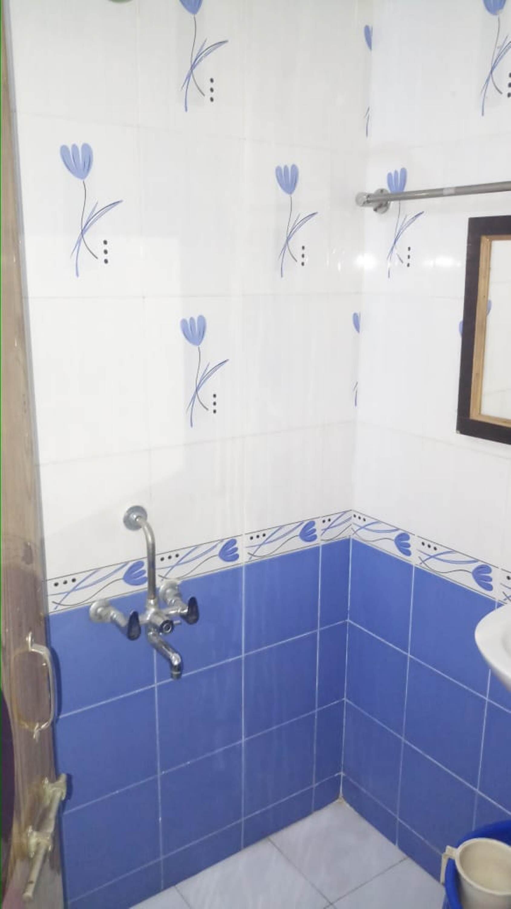 A bathroom with white and blue tiles, a shower with a handheld showerhead, and a small sink.