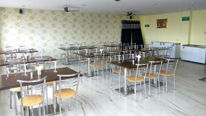 A dining hall with multiple tables and chairs, ceiling fans, and a refrigerator. - Arjun Pride Hotel (Baramati)
