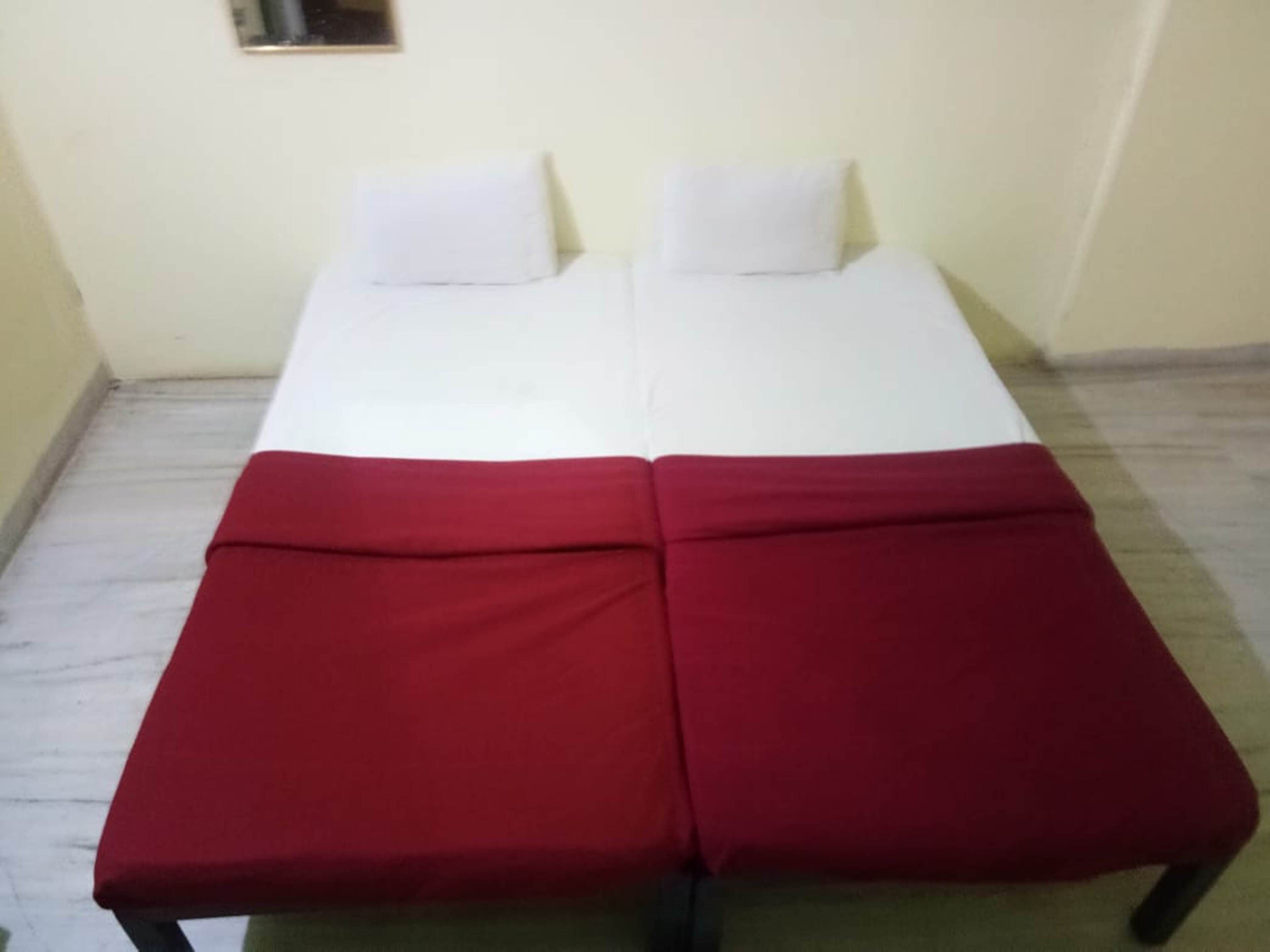 A double bed with white bedding and two pillows, a red blanket on the floor, and a small mirror on the wall.