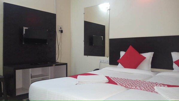 A hotel room with a bed, a TV mounted on the wall, and a bedside table. - Arjun Pride Hotel (Baramati)