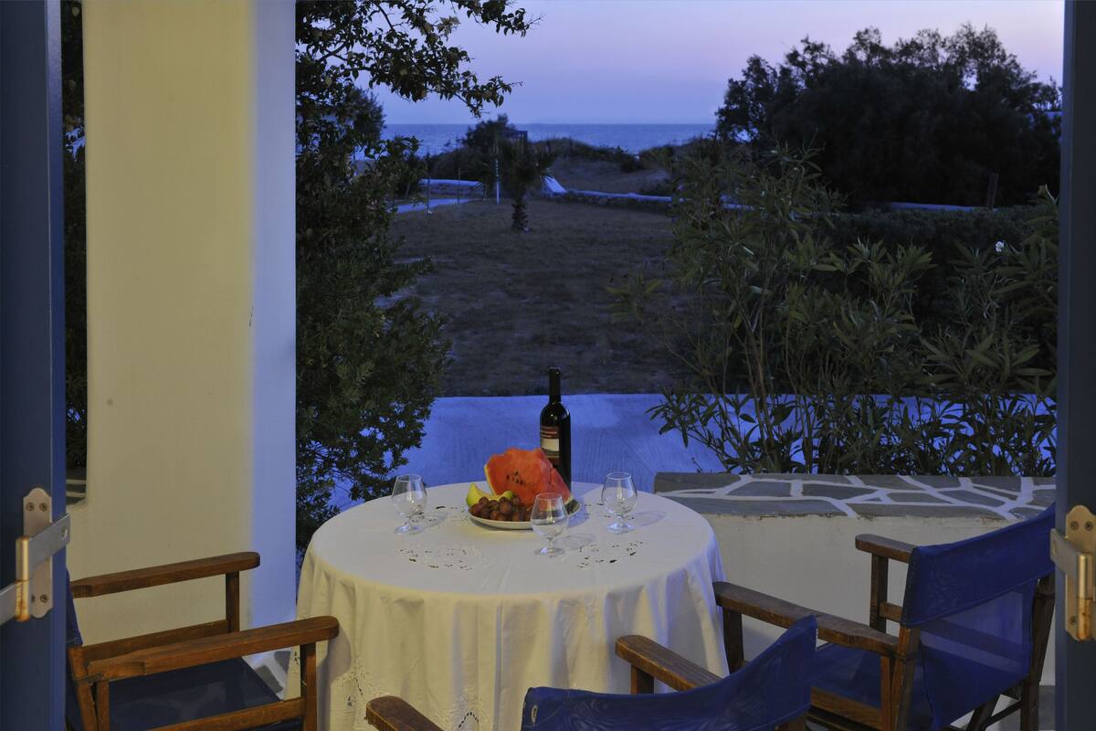 A table set for two with a bottle and a plate of fruit, overlooking a beach.