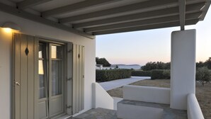 A covered outdoor area with a stone floor, a white wall, and a door with glass panels. - Golden Sand Paros (Paros)