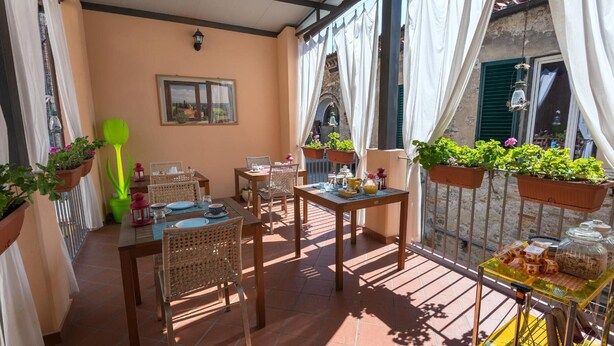 Un balcón con mobiliario de mimbre, plantas en macetas y una mesa con alimentos para el desayuno.
