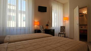 A hotel room with two beds, a desk with a lamp, a chair, and a TV mounted on the wall.