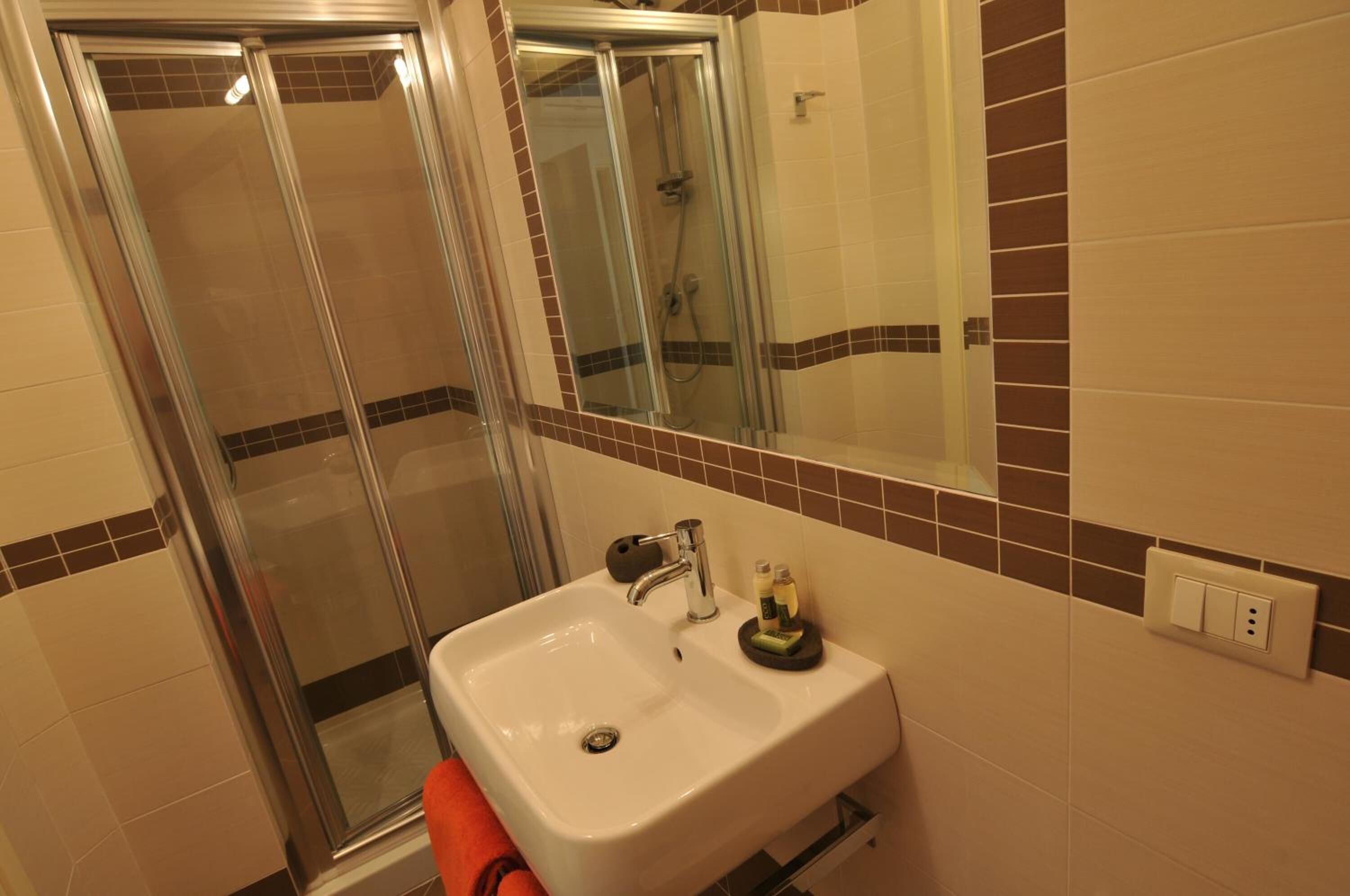 Une salle de bain avec une douche à parois de verre, un lavabo blanc avec un miroir au-dessus, et un mur carrelé avec une bordure marron.