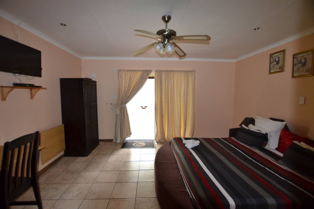 A hotel room with a bed, a desk, a television, a ceiling fan, and a door leading to the outside.