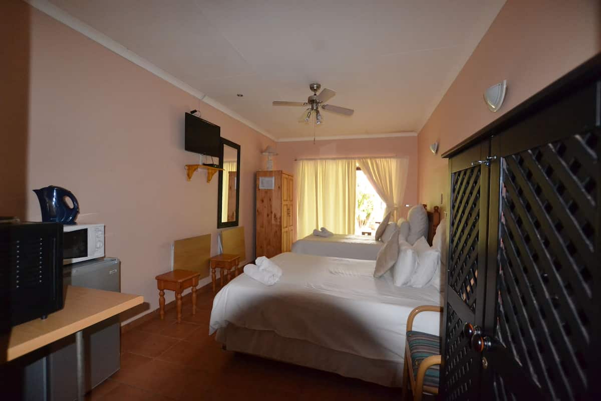 A hotel room with a bed, a desk with a computer, a chair, a wardrobe, and a ceiling fan.